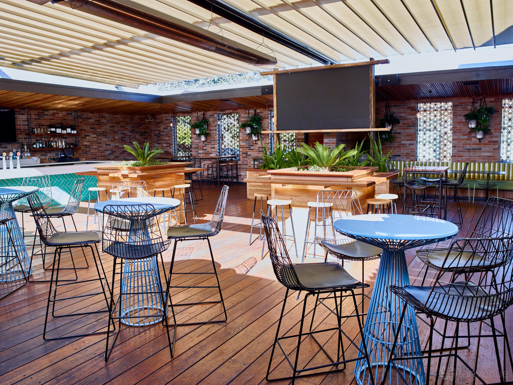 An open-air pub event space with wire chairs, round tables, brick walls, and a retractable roof at The Precinct Hotel courtyard.