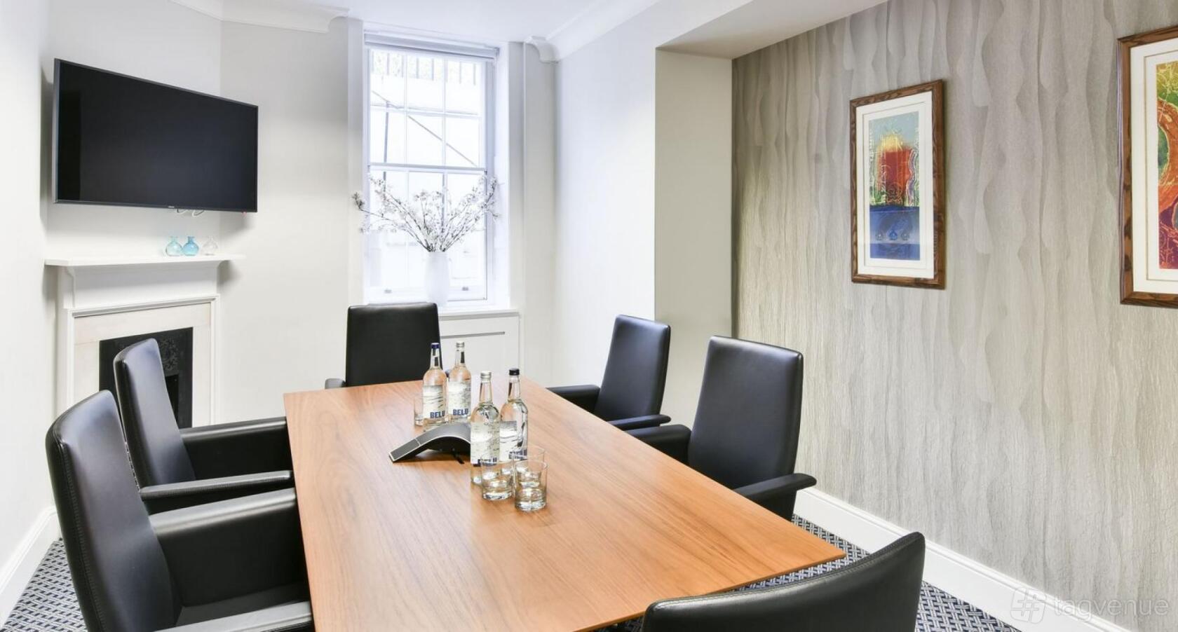 A meeting room with a wooden conference table, black chairs, and a wall-mounted TV at 21 Gloucester Place.