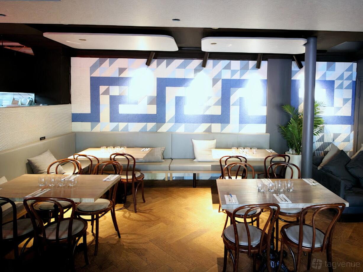 A hotel bar with wooden tables, bentwood chairs, bench seating, and geometric blue wall art at Phoenix Hotel.