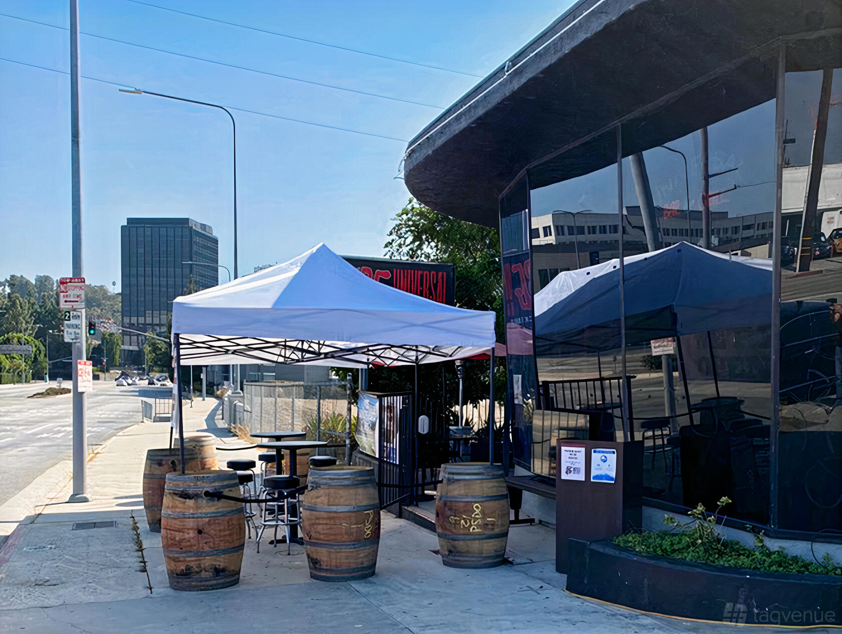 A bar terrace with canopy tents, round tables, and barrel seating on the patio at Universal Bar and Grill.