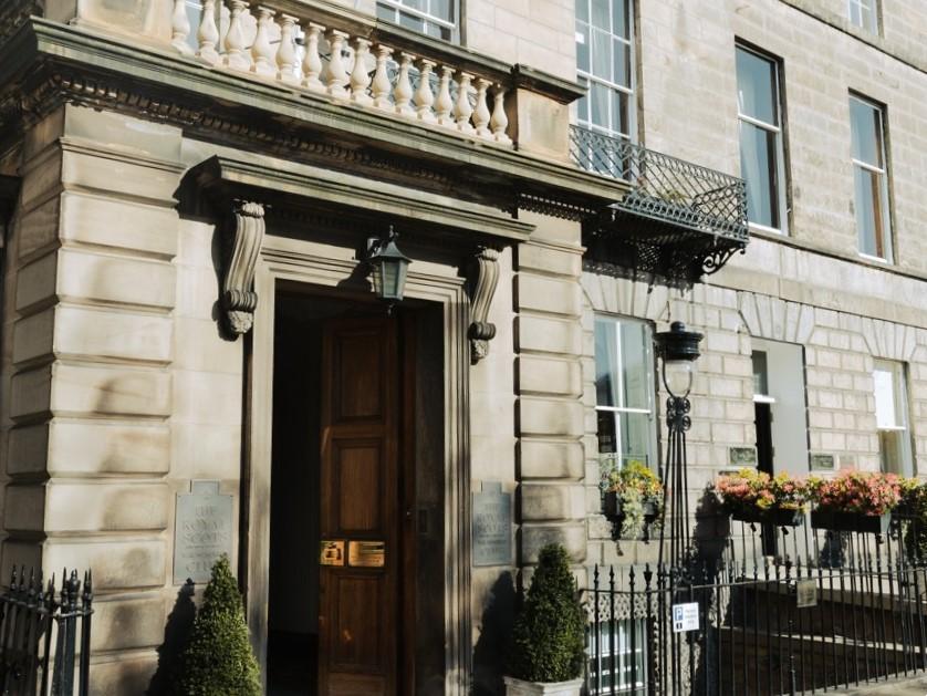 A hotel entrance with stone columns, a wooden door, balcony, and flower boxes at Royal Scots Club.