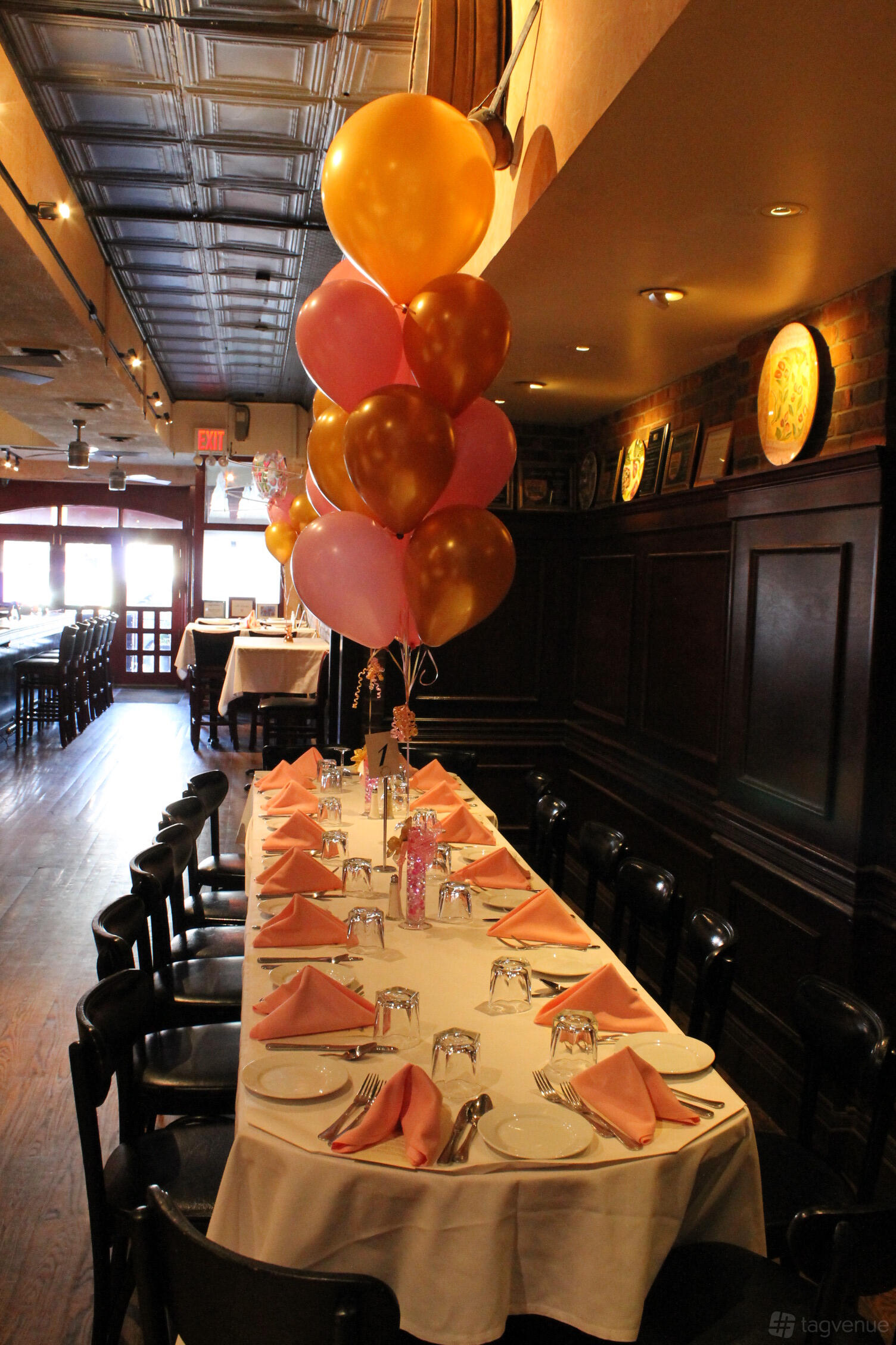 A restaurant with a long table set with pink napkins, glassware, and pink and gold balloons at Papazzio.