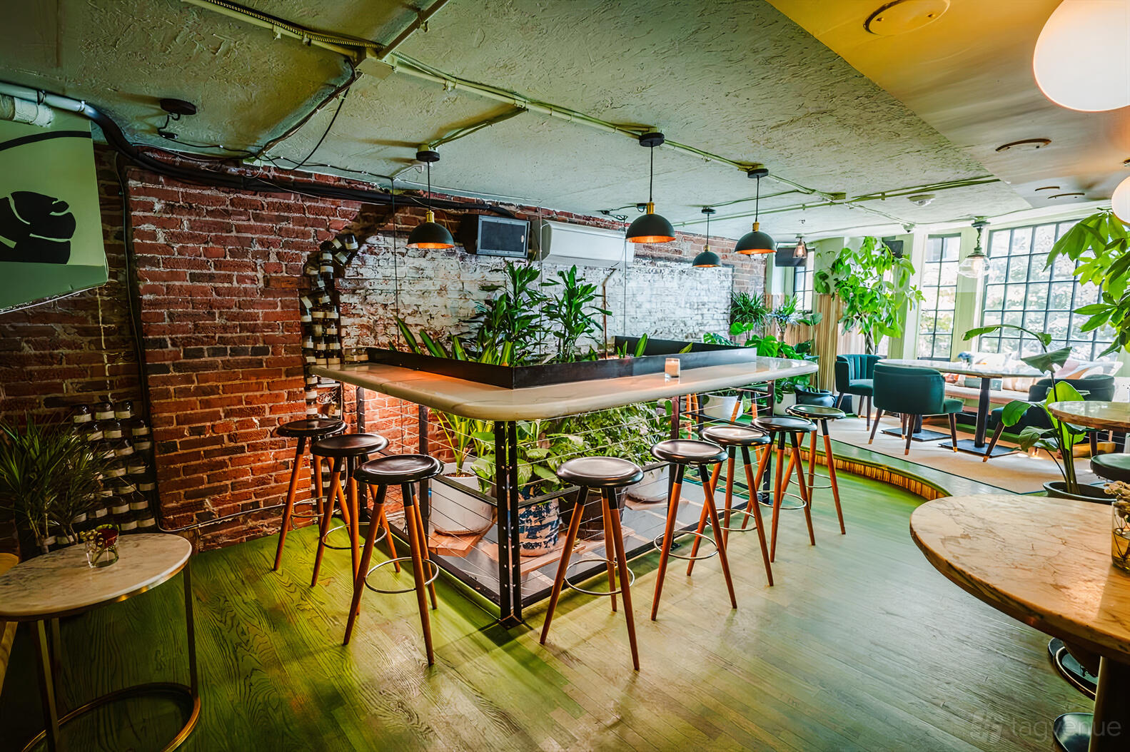 A dining room with exposed brick walls, hanging pendant lights, and leafy plants at Residents Cafe & Bar.