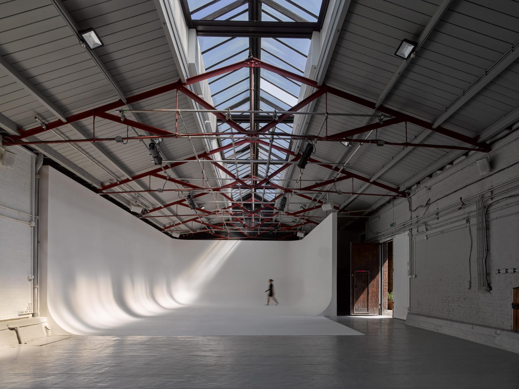 A photo studio with high ceilings, skylights, and a large white cyclorama wall at Park Village Studios.