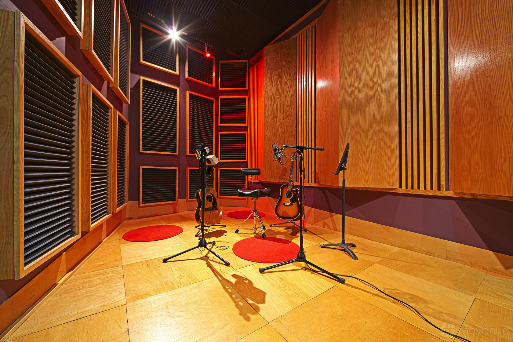 A recording studio with acoustic panels, wood flooring, two guitars, and microphones set up at Empire Sound Studio.