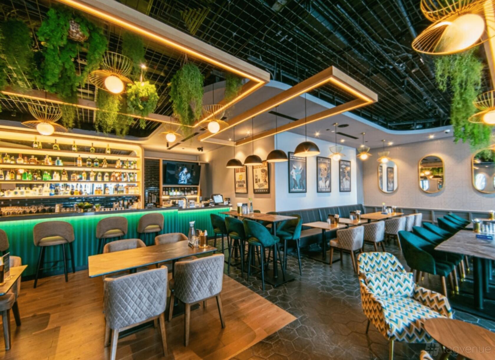 A restaurant with greenery hanging from the ceiling, upholstered seating, and a backlit bar at Social Bar & Bistro.
