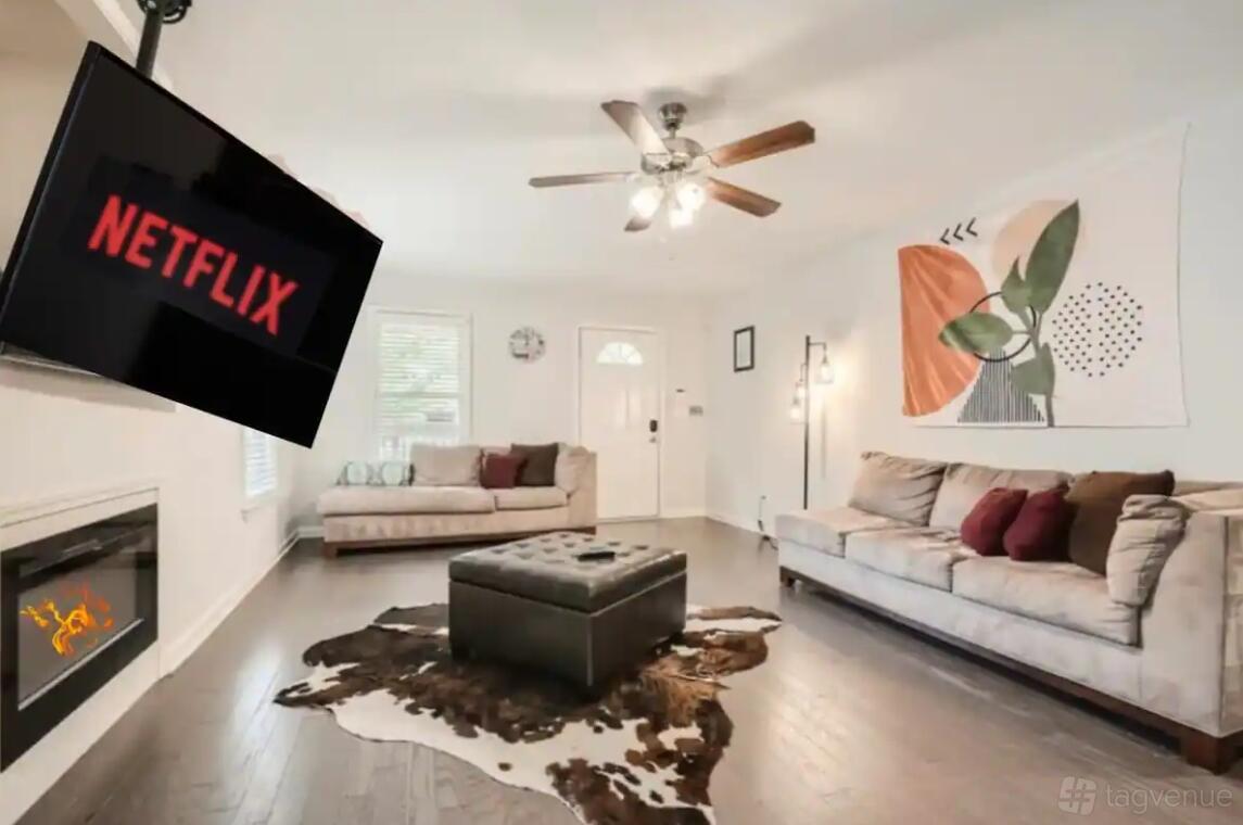 A house living room with two beige sofas, a mounted TV, ceiling fan, cowhide rug, and wall art at Spacious 4 Bedroom Home | Heart of ATL.