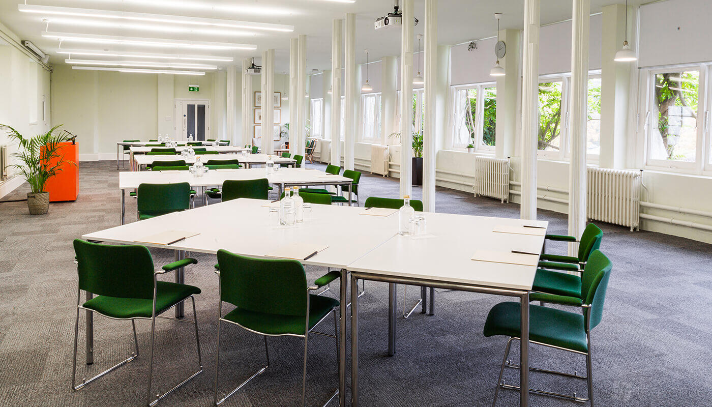 An event space with white tables, green chairs, and large windows letting in natural light at Ashridge House.
