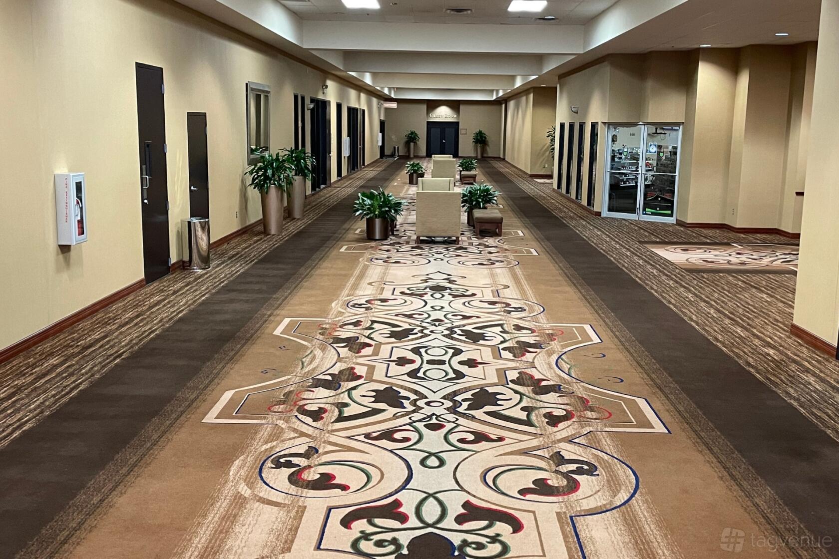 An event foyer with ornate carpeting, potted plants, beige walls, and cushioned benches at The Community Collective for Houston.
