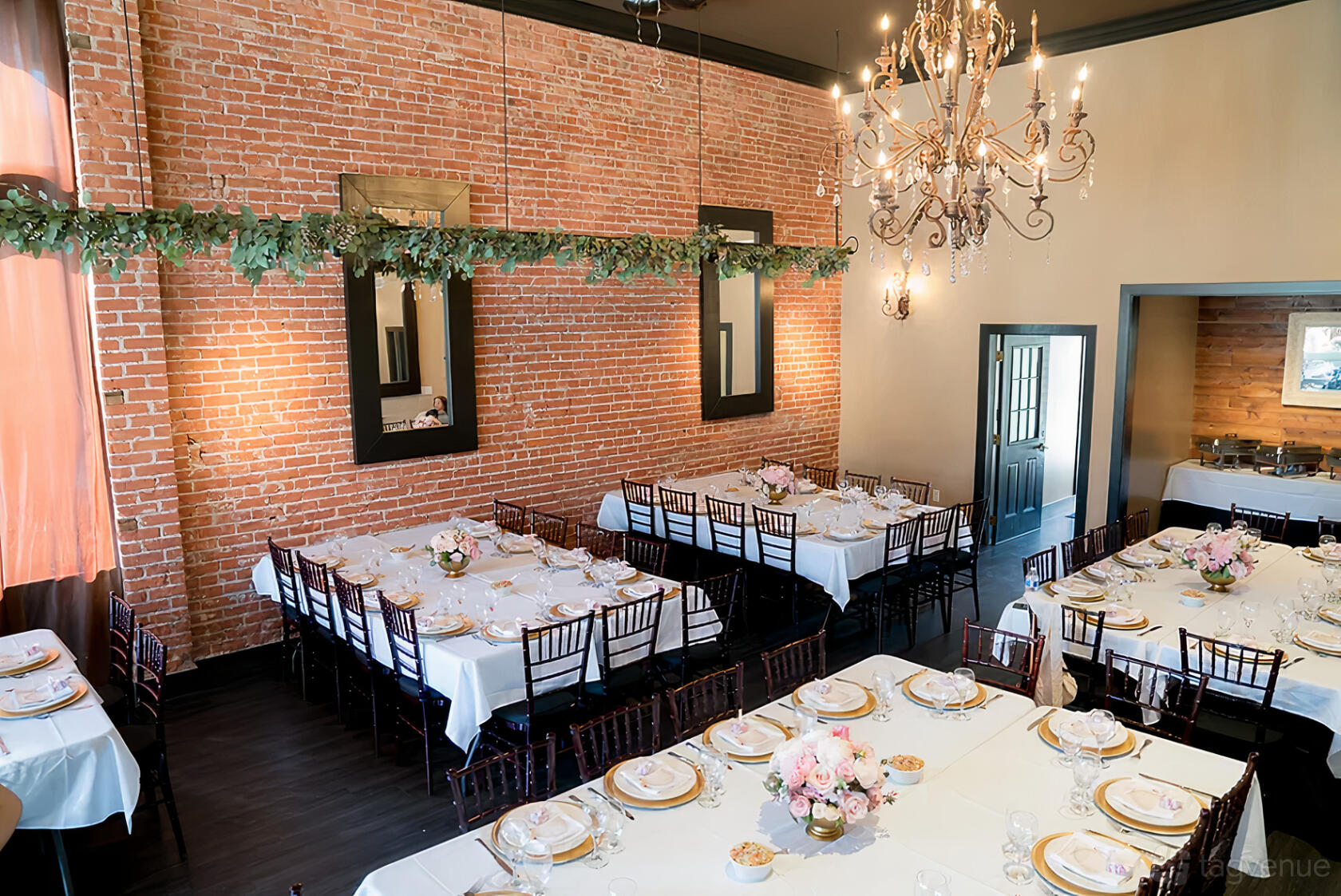 A function room with exposed brick walls, chandeliers, and banquet tables set with white linens at Pinocchio's Pizza.