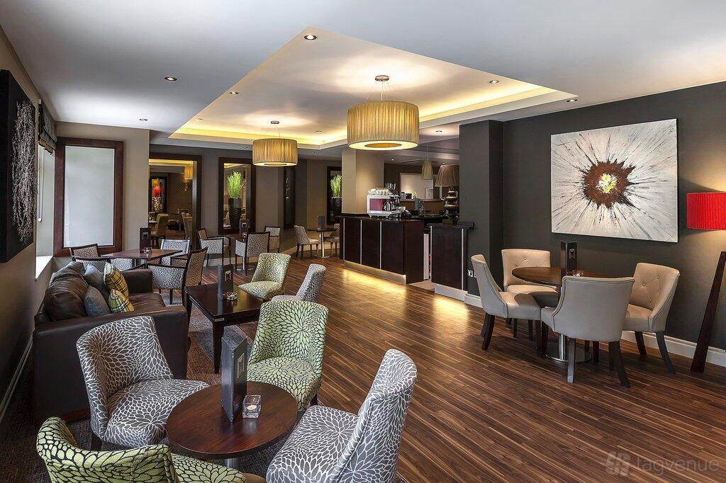 A hotel restaurant with patterned armchairs, wooden floors, and contemporary lighting at Pinewood on Wilmslow.