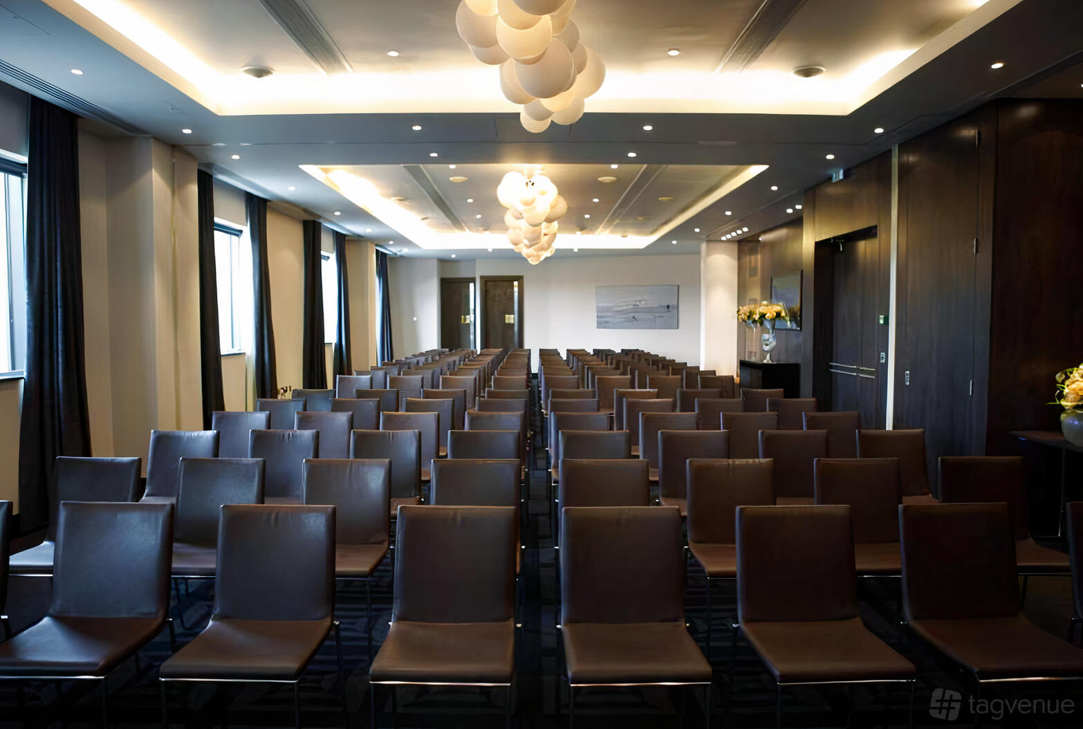 A meeting room with rows of brown chairs, large windows, and modern ceiling lights at Brooklands Hotel.
