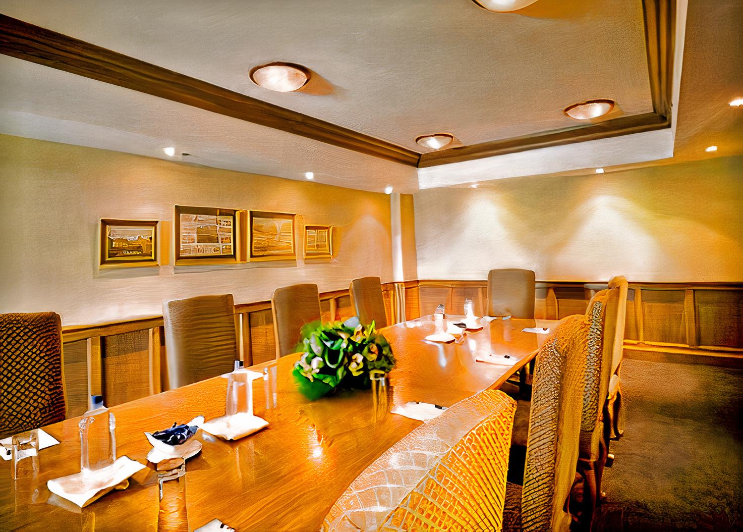 A hotel boardroom with a large wooden table, cushioned chairs, wall art, and ceiling lights at Pullman & Mercure Melbourne Albert Park.