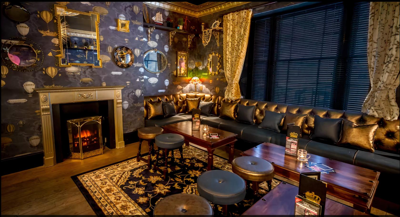 An event space with a patterned rug, leather sofas, dark wood tables, and an ornate fireplace at The Cocktail Club Triangle.