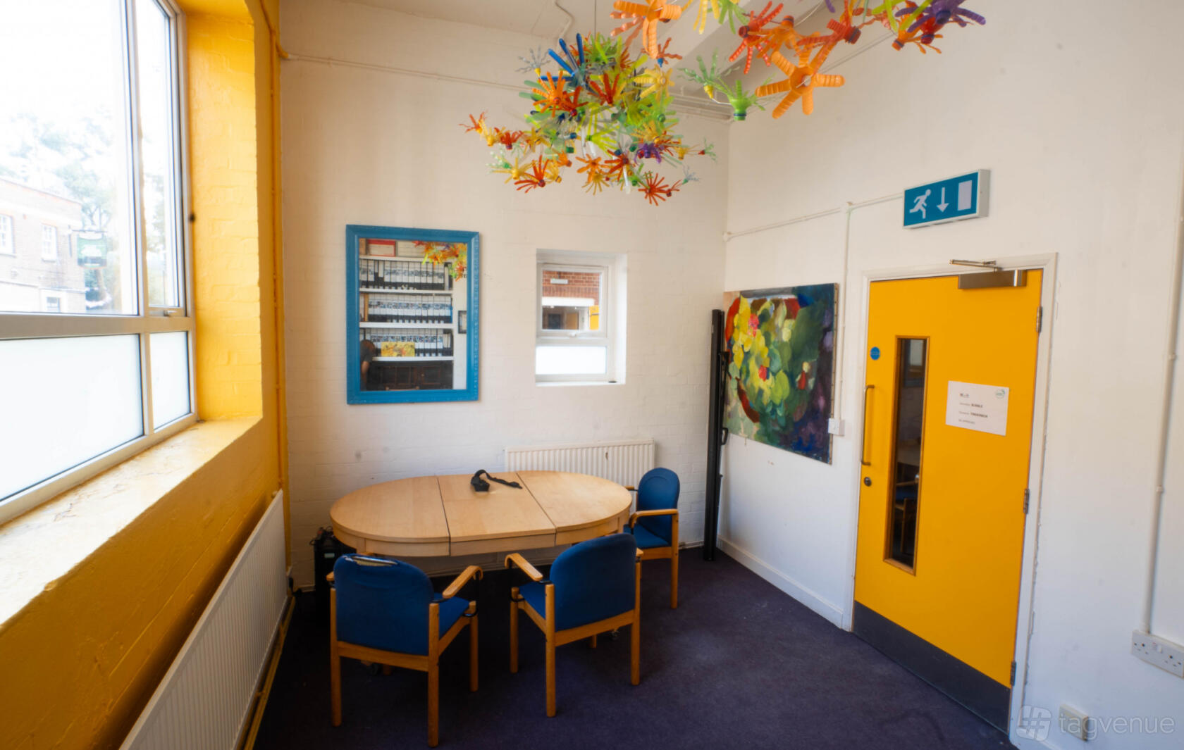 A meeting room in a theatre with a round table, blue chairs, colorful ceiling art, and bright yellow accents at London Bubble Theatre.