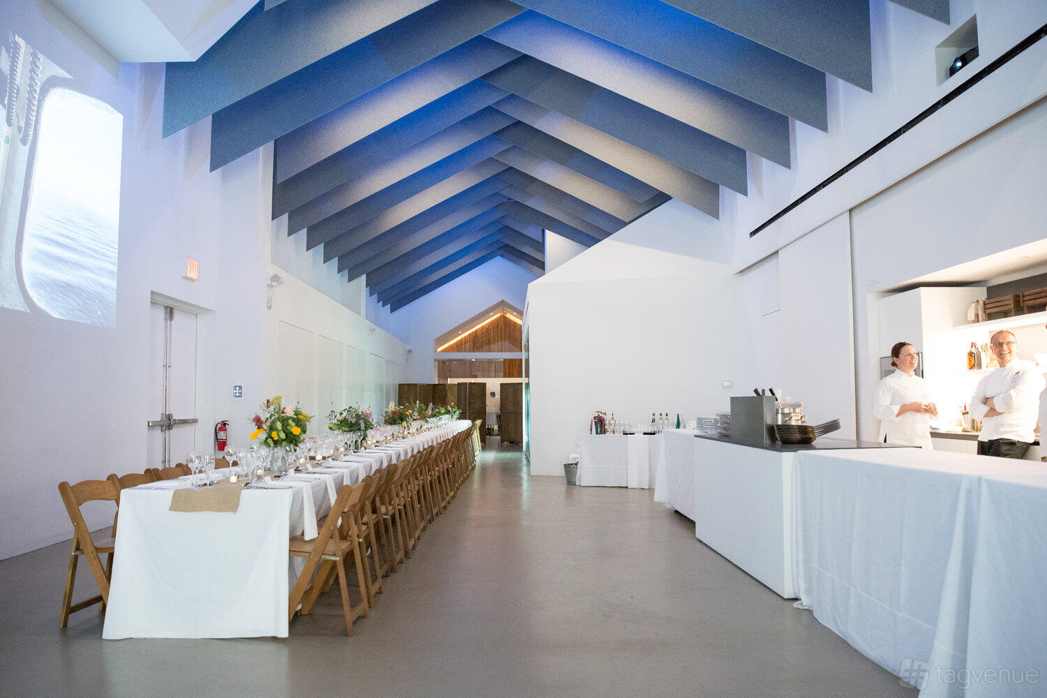 An event venue with vaulted ceilings, a long banquet table with white linens, and a built-in bar at Project Farmhouse.