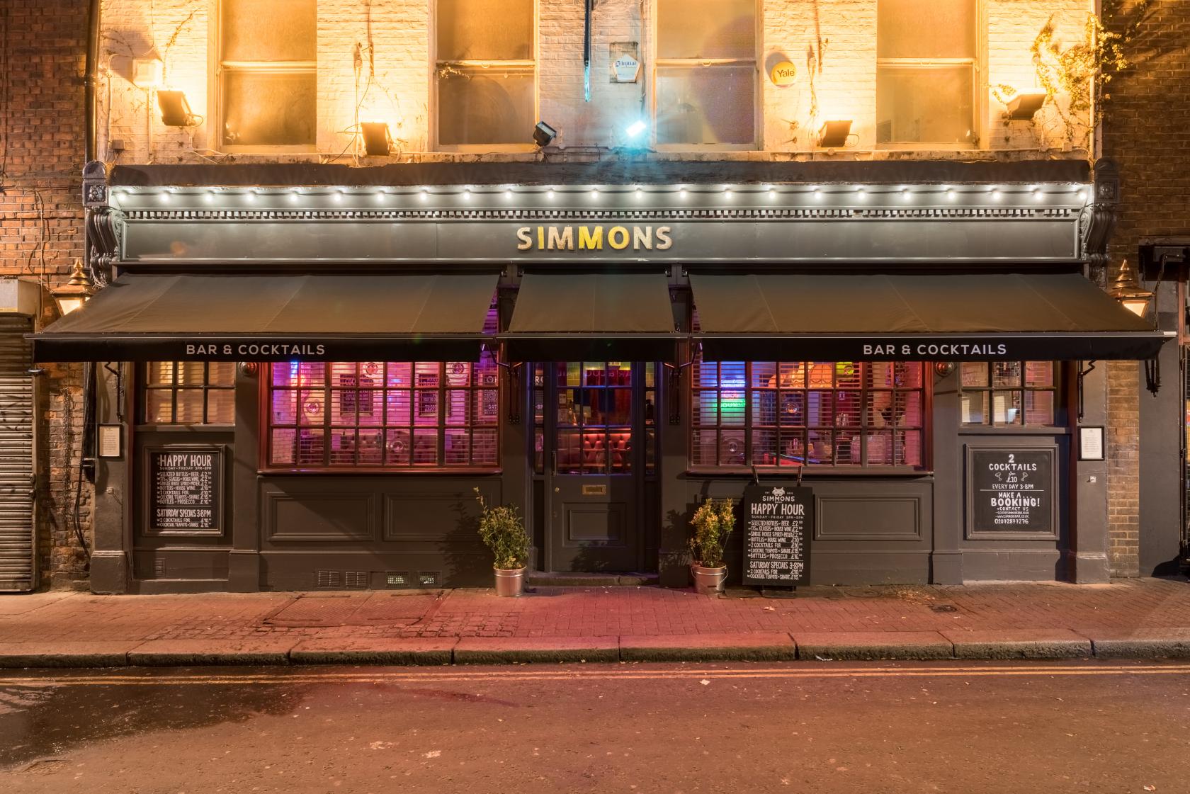 A pub with illuminated signage, brick facade, and large front windows at Simmons | Soho.