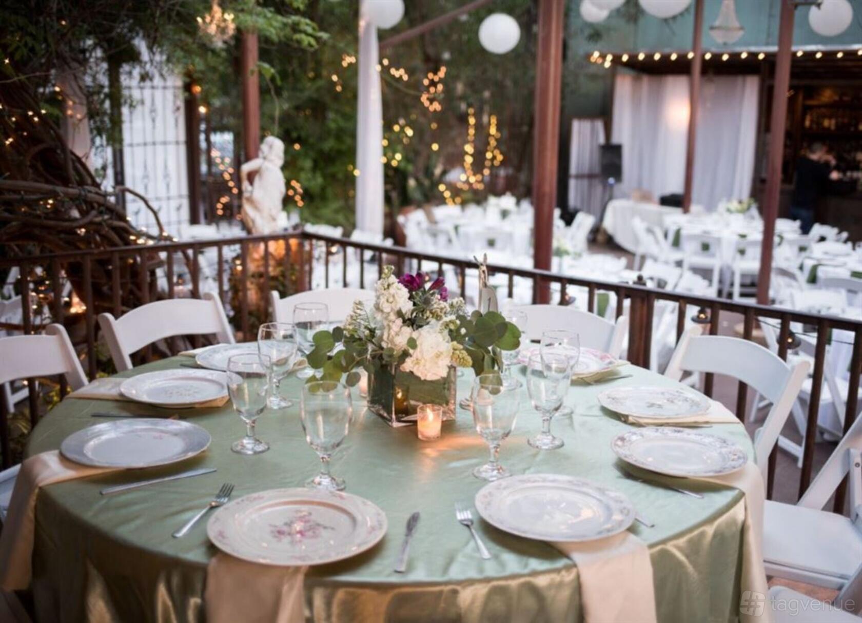 A terrace with round tables covered in green linens, floral centerpieces, and string lights at AvantGarden.