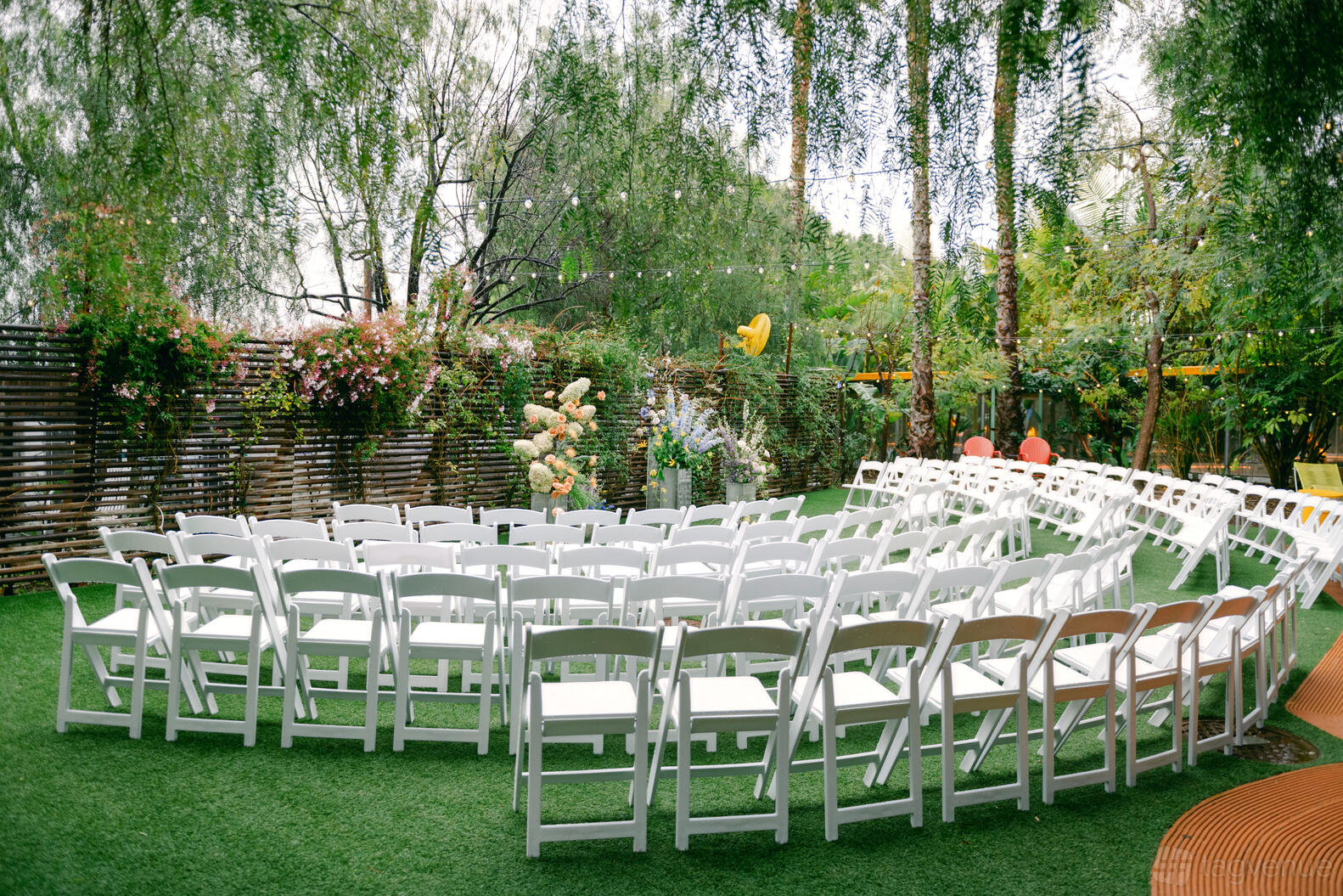 A garden with white folding chairs arranged in rows on green grass and string lights above at The Preserve.