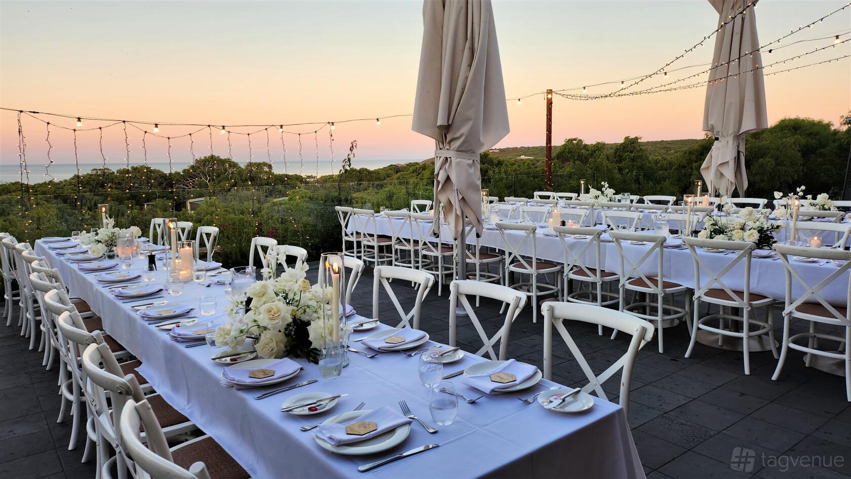 A restaurant terrace with long tables covered in white linens, floral centerpieces, and string lights at Pullman Bunker Bay.