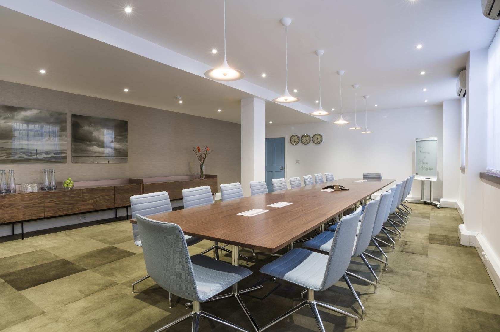 A boardroom with a long wooden table, grey swivel chairs, and floor-to-ceiling windows at The Derby.