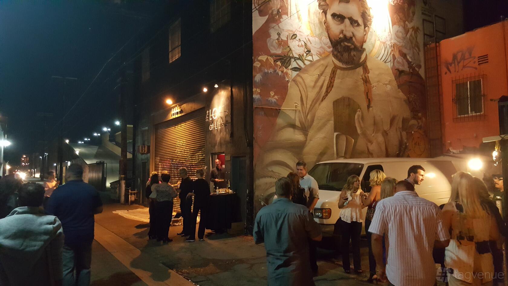 An art gallery entrance with a large mural on the exterior wall and people gathered outside at NYC style Loft Art Gallery.
