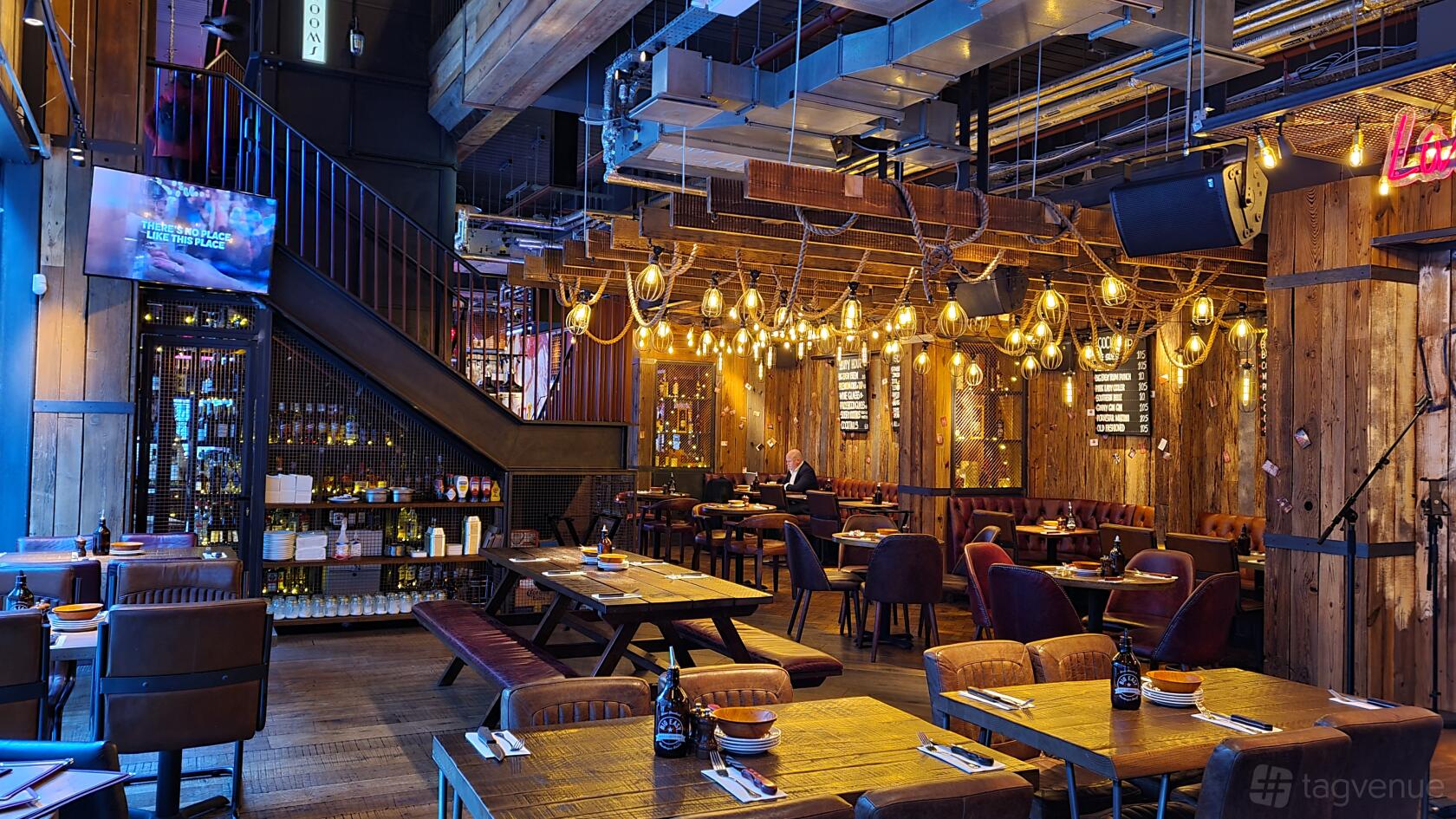 A restaurant with exposed ceilings, wooden walls, hanging globe lights, and mixed seating at BIG EASY - Westfield Stratford.