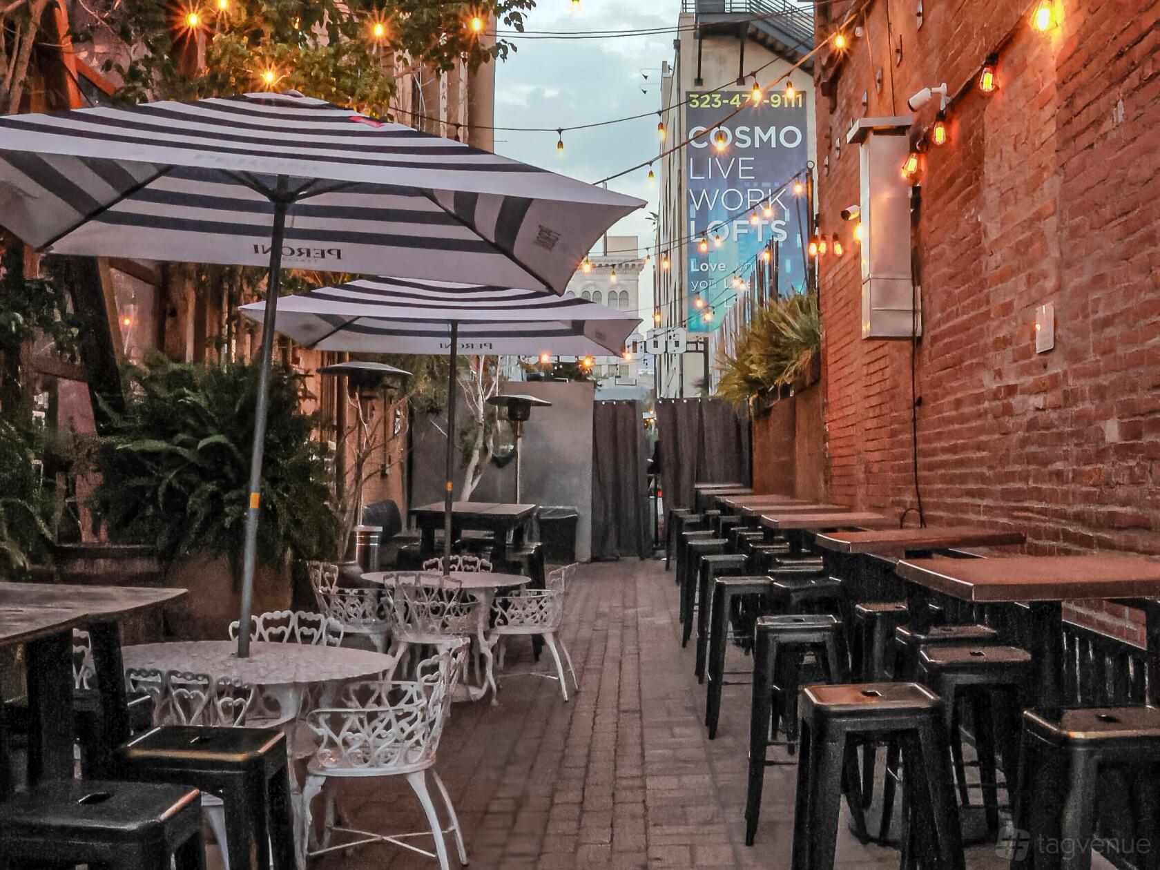 A terrace with striped umbrellas, exposed brick walls, and string lights at Saint Felix Hollywood.