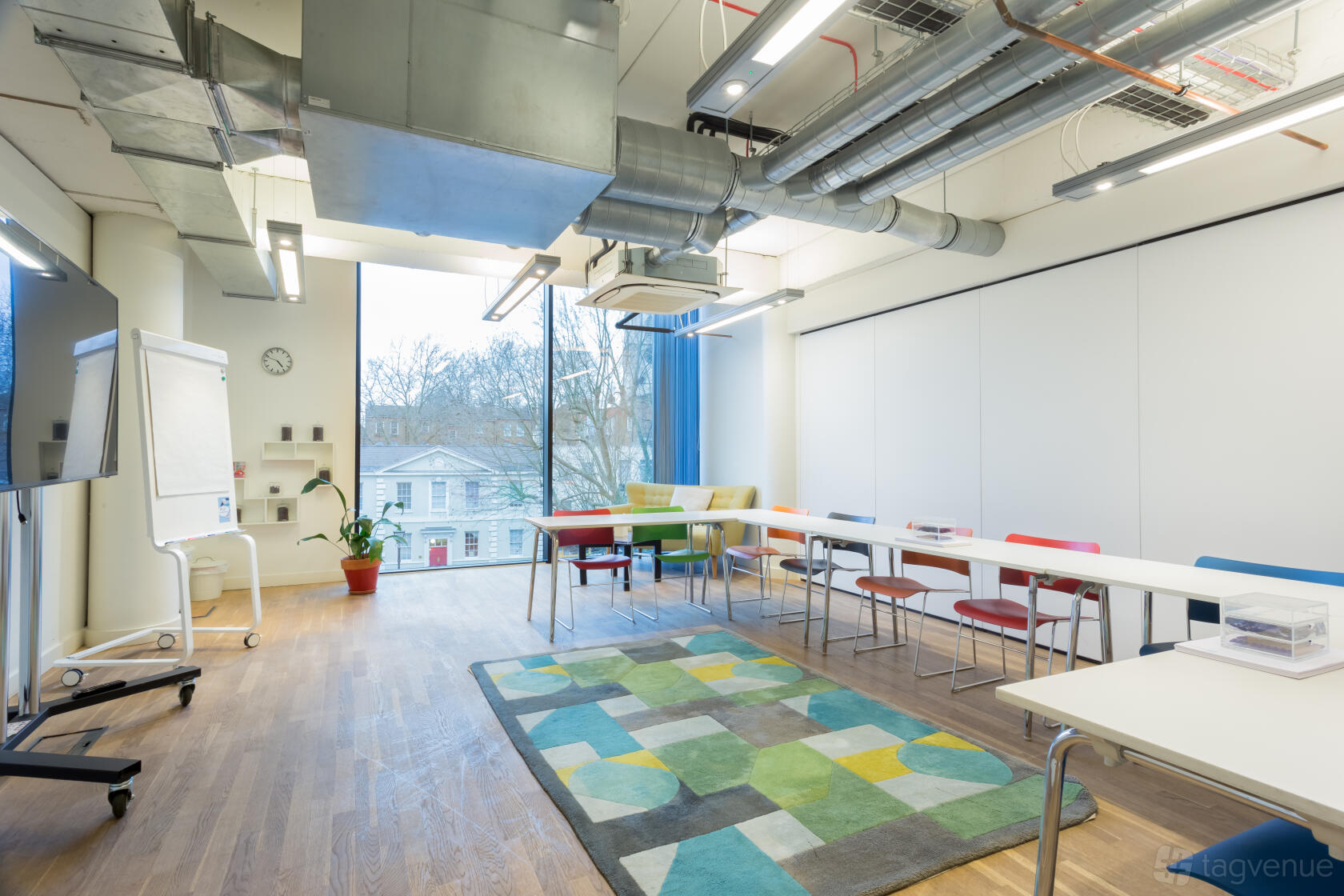 A training room with U-shaped tables, colorful chairs, large windows, and exposed ductwork at Wallacespace Clerkenwell Green.
