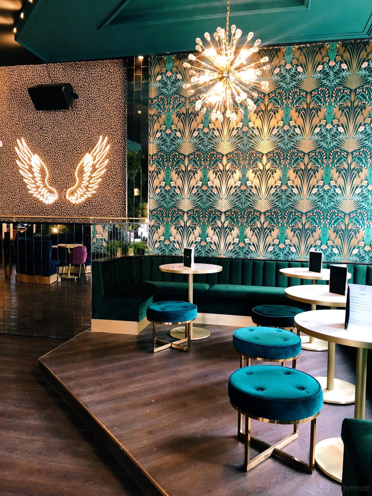 An event space in a cocktail bar with green velvet seating, round tables, and art deco wallpaper at Lost Society (Battersea SW11).