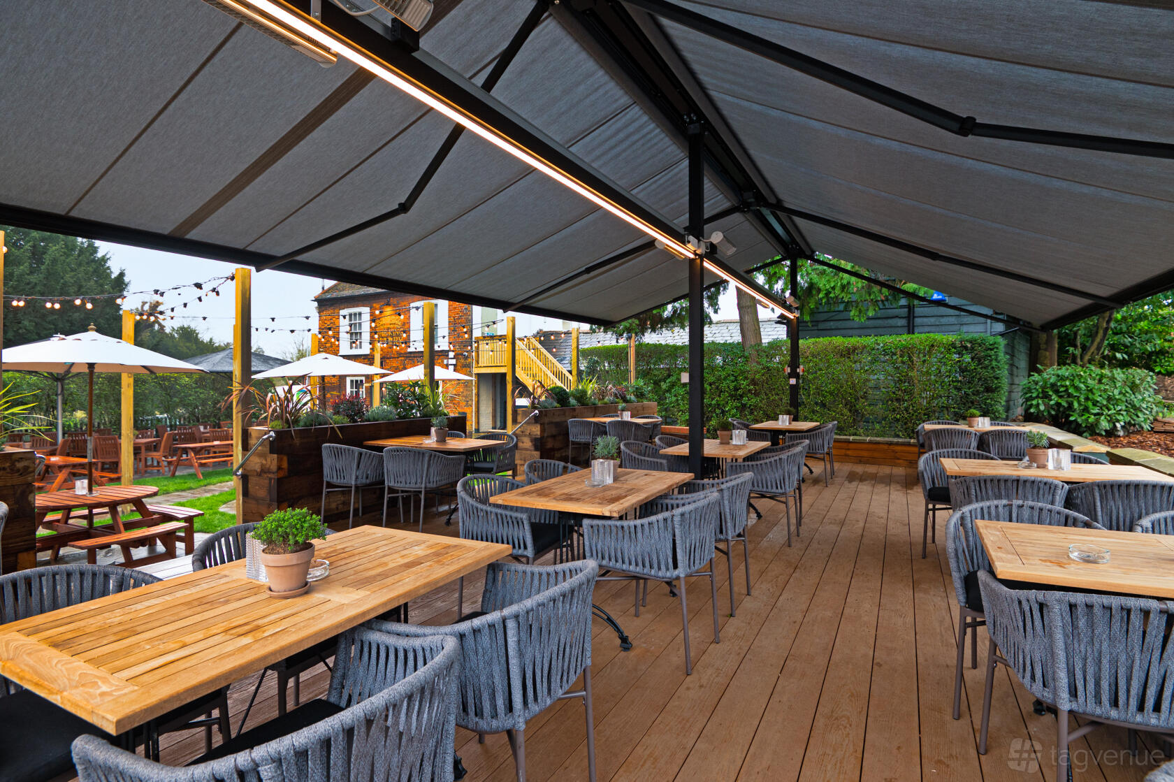 An outdoor pub seating area with wooden tables, woven chairs, and large canopies at The King Harry.