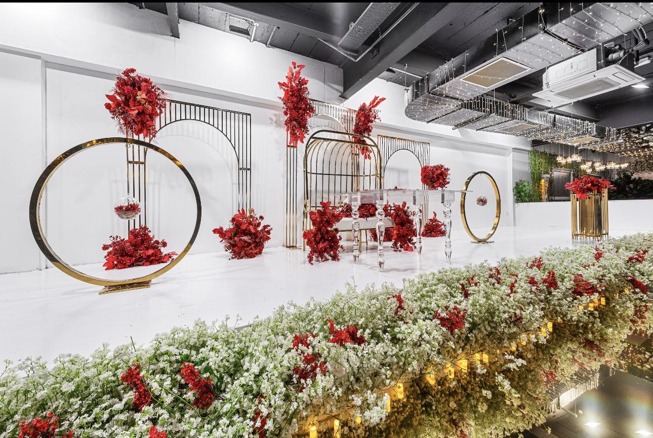 A banqueting hall with a white stage, gold arches, and red floral arrangements at Eden Experiences.