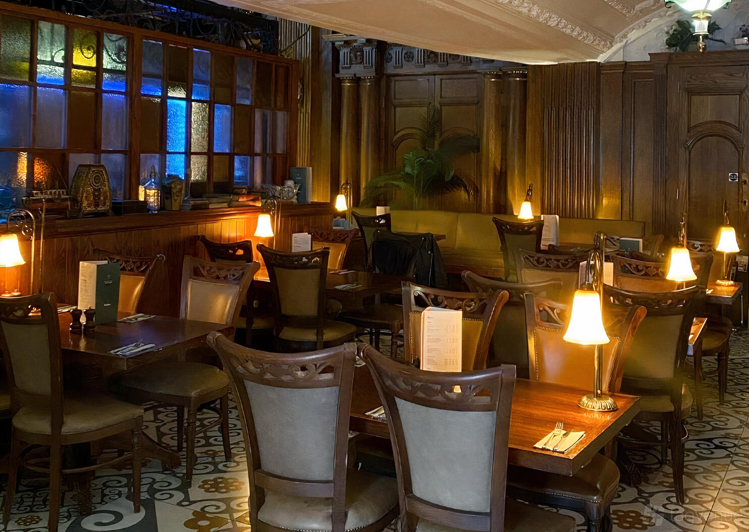 A restaurant with wooden tables, upholstered chairs, warm table lamps, and stained glass accents at The Trading House.