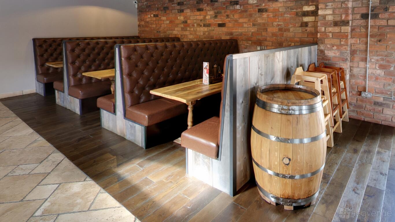 A restaurant with brown leather booths, wooden tables, a barrel accent, and exposed brick walls at The Koyla Kitchen @ The Thorns.