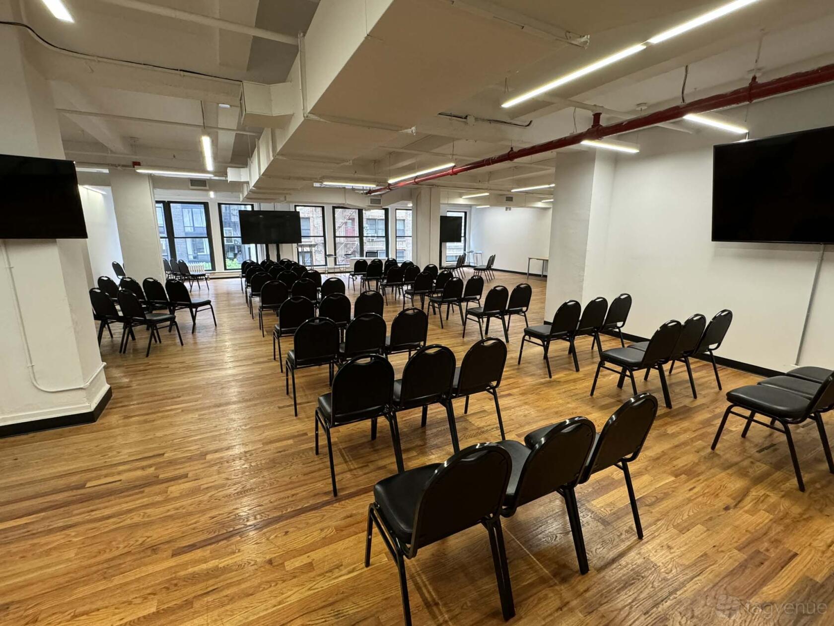 A meeting hall with rows of black chairs, wood flooring, and large windows at NYC Seminar & Conference Center.