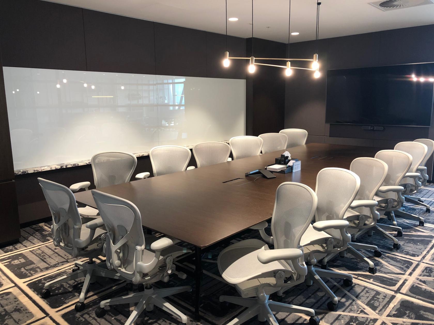 A coworking space with a long conference table, ergonomic chairs, a large whiteboard, and a TV at Collins Square.