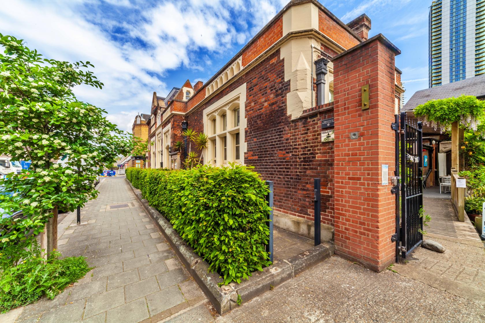 A historic building with red brick exterior, arched windows, and surrounding greenery at Jamyang Buddhist Centre.