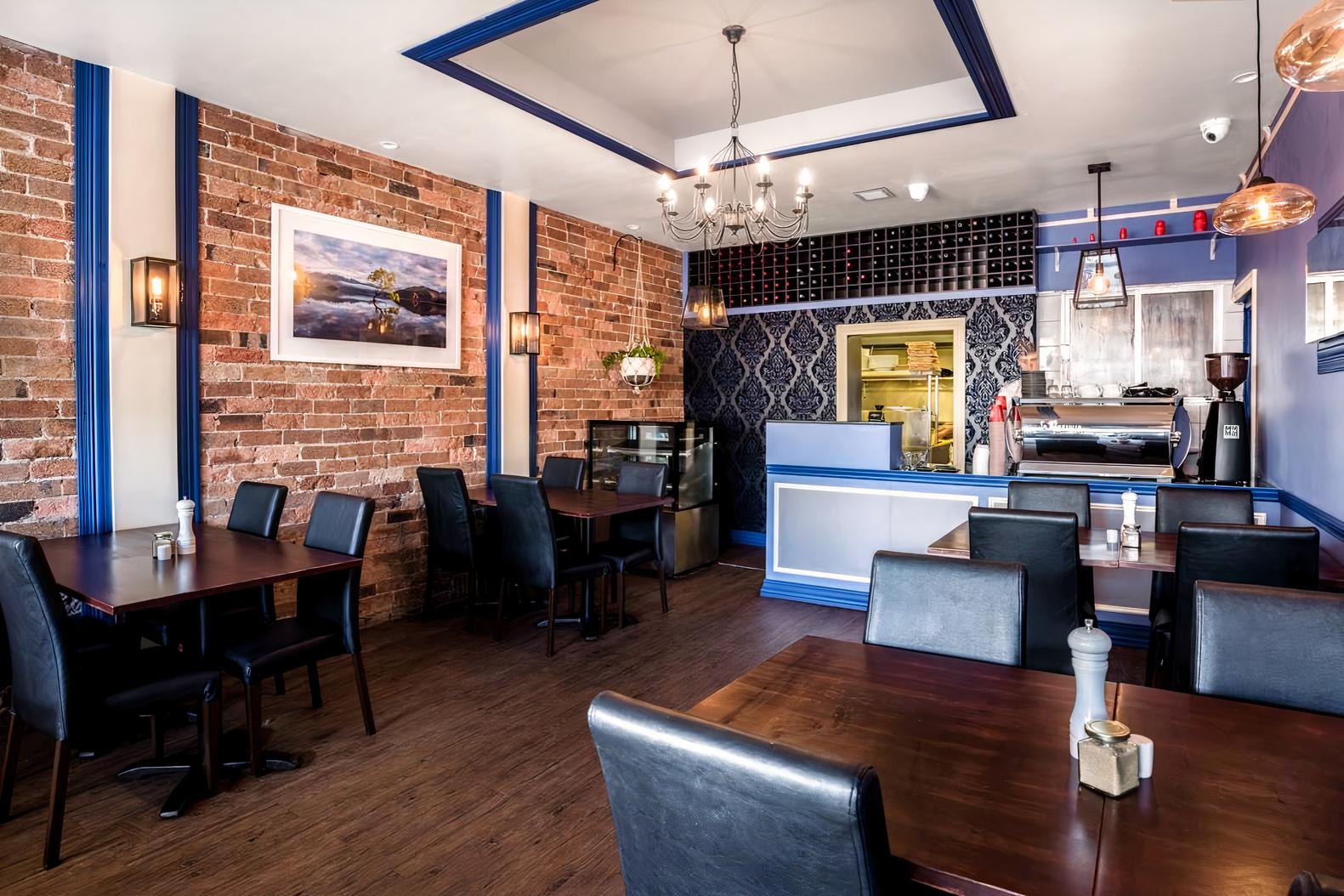 A restaurant with exposed brick walls, dark wood tables, leather chairs, and a wine rack behind the bar at The Peppertree Restaurant.