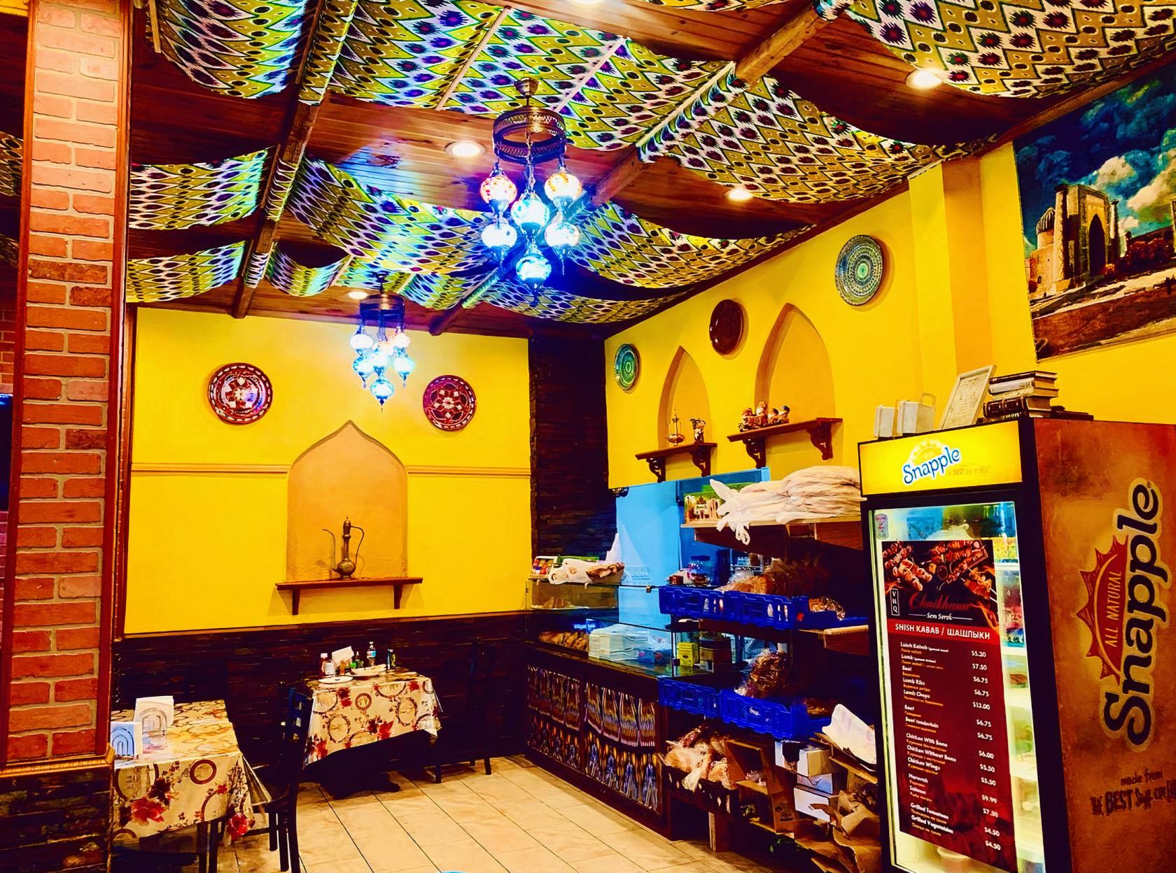 A restaurant with patterned fabric ceiling, hanging lanterns, yellow walls, and decorative shelves at Chaikhana Sem Sorok.