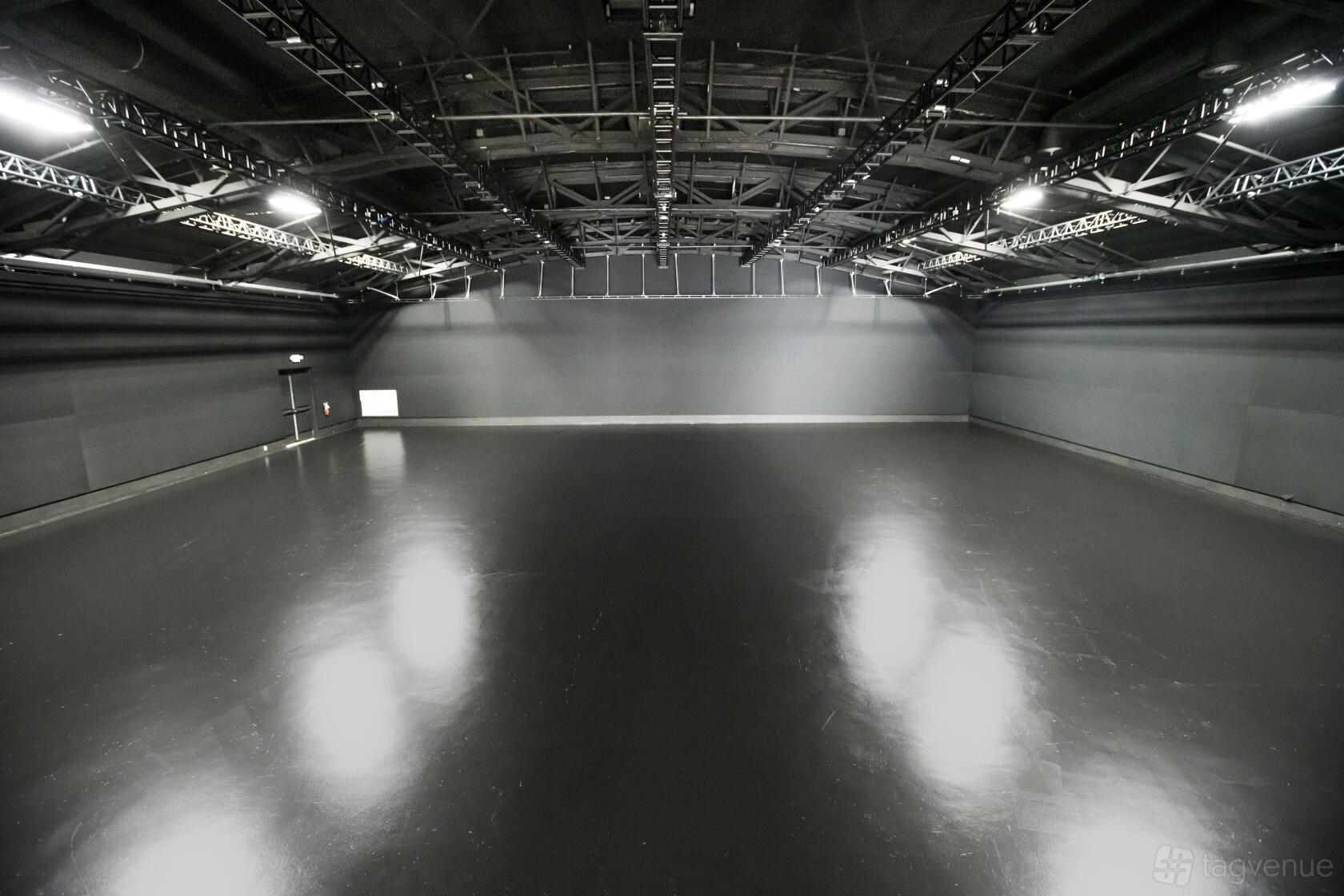 A photo and film studio with high ceilings, exposed trusses, and polished black floors at Optimist Studios.