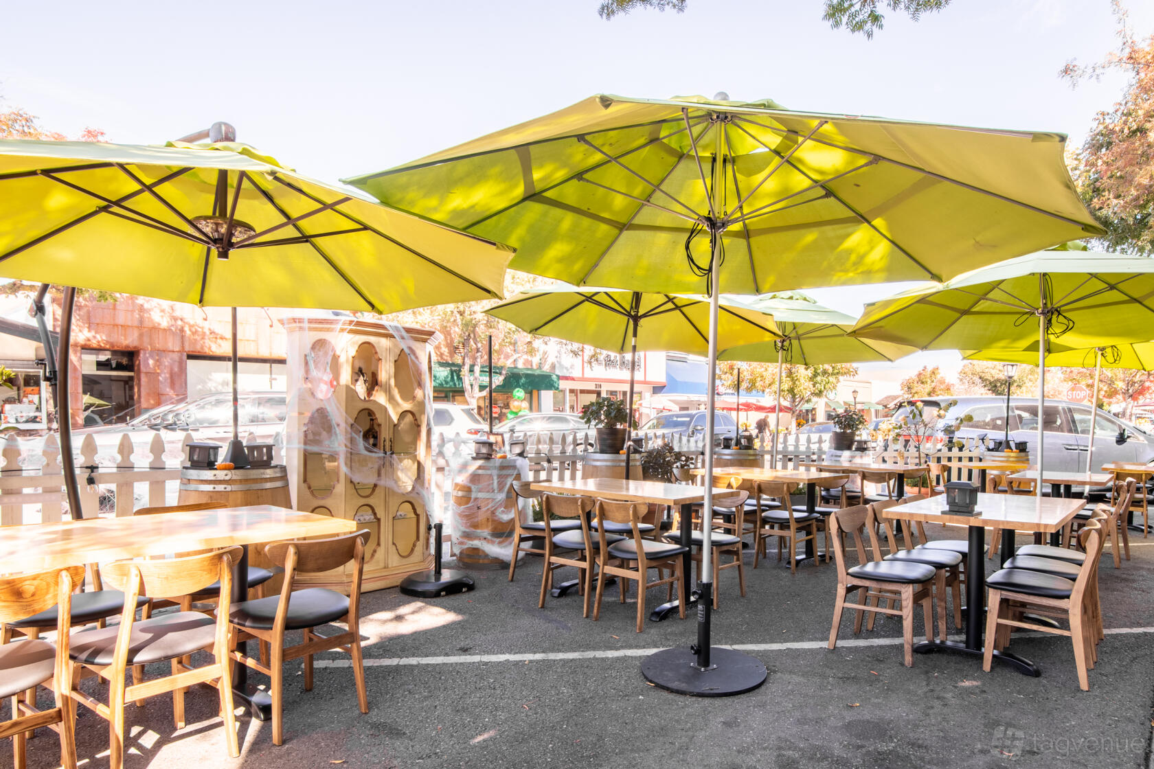 An outdoor restaurant patio with wooden tables, matching chairs, and large green umbrellas at Venue name.