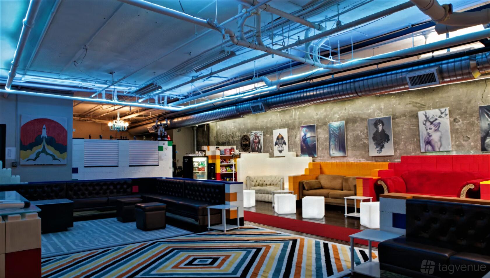 An event room with geometric patterned carpet, colorful seating, exposed ductwork, and illuminated cube tables at Alley Mic.