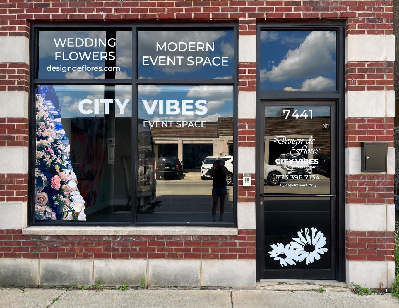 A brick facade with large storefront windows featuring floral graphics and signage at City Vibes Event Space.