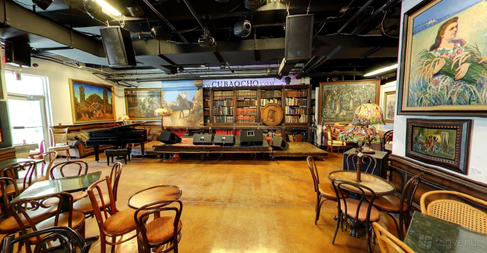 A museum event space with vintage wooden chairs, a stage, bookshelves, artwork, and a grand piano at Cubaocho Museum & Performing Arts Center.