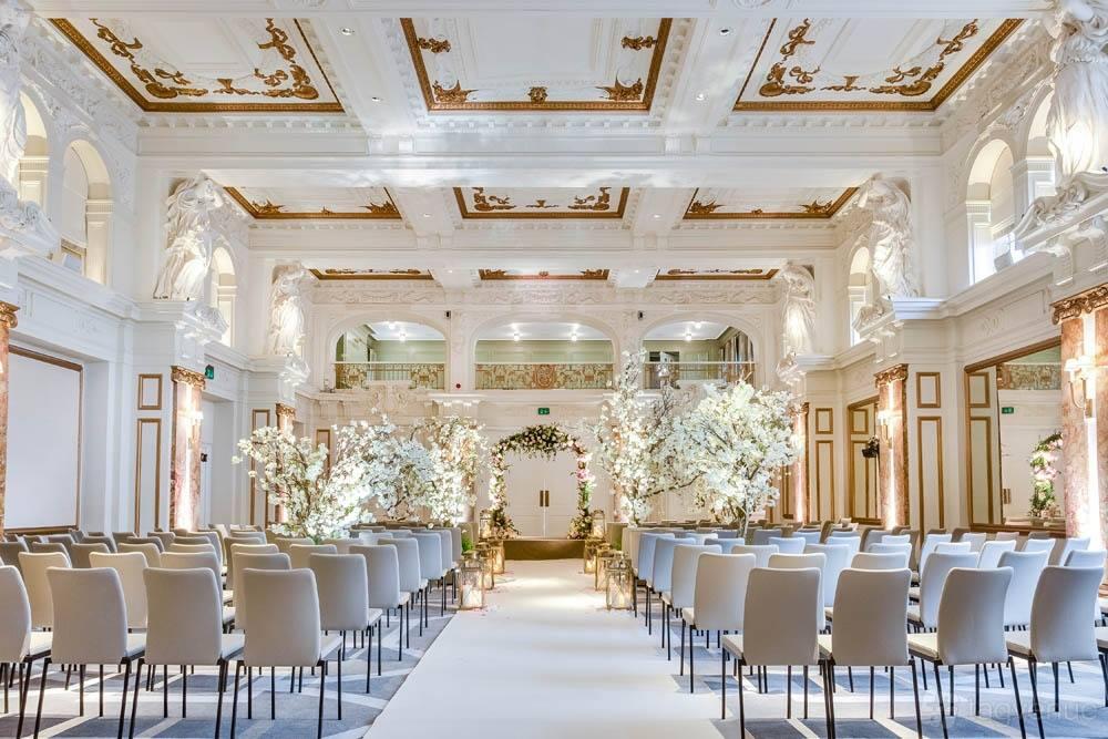 A ballroom with ornate ceilings, marble columns, and rows of chairs arranged for a ceremony at Kimpton Fitzroy London.