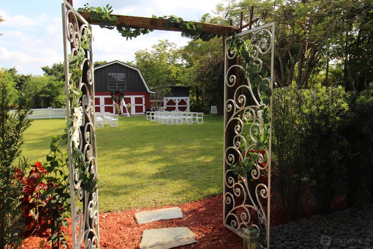 An event venue with a red barn, white ceremony chairs on lawn, and decorative wrought iron gates at Pleasant Garden.