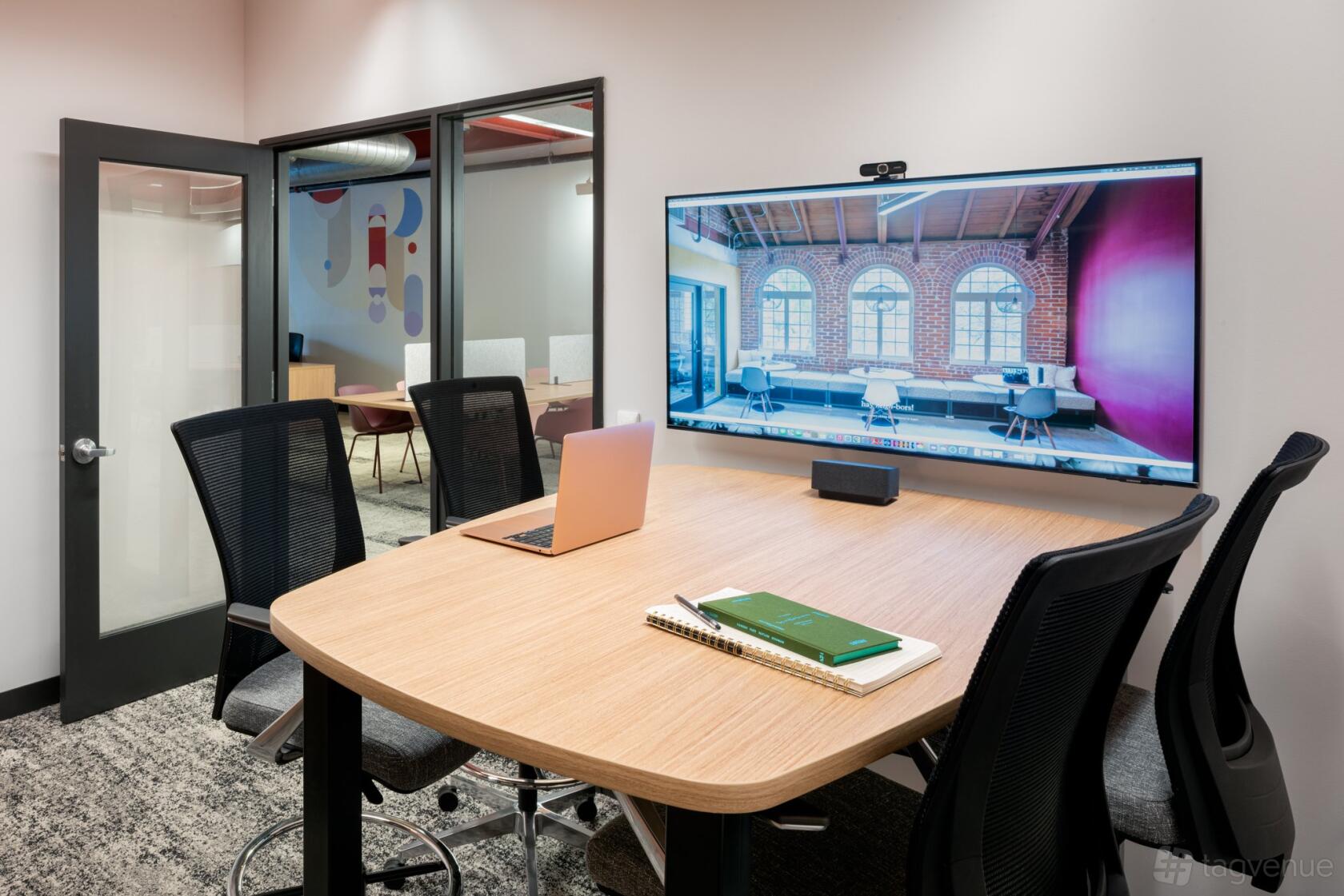 A meeting room with a rectangular wooden table, mesh chairs, and a wall-mounted screen at Livery Studio.
