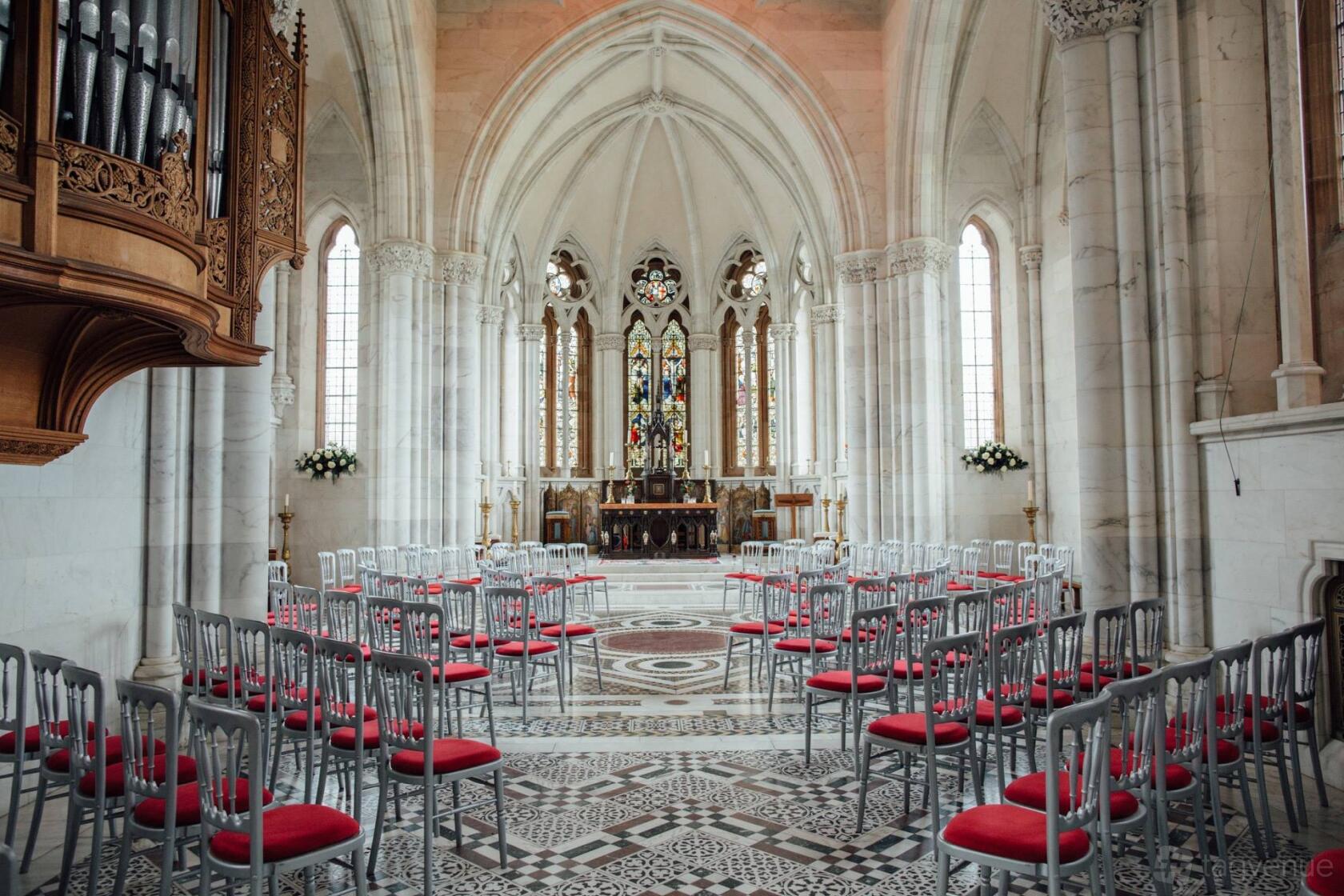 A historic building with vaulted ceilings, stained glass windows, and arranged chairs with red cushions at Mount Stuart.