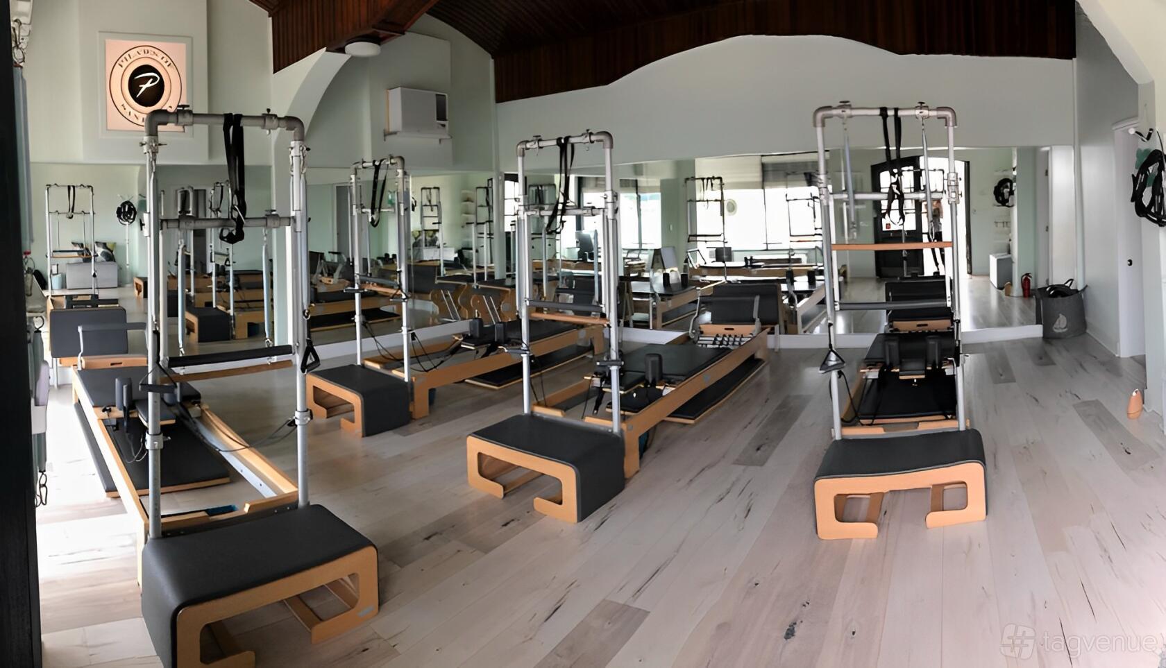 A dance studio with mirrored walls, light wood flooring, and multiple pilates reformer machines at Pilates of San Diego - Del Mar.