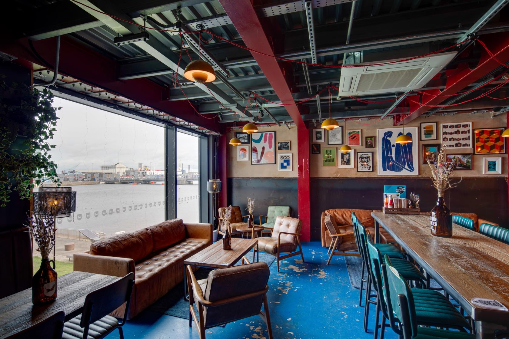 An event space in a bar with large windows, blue floors, mixed seating, and eclectic wall art at BrewDog Outpost Dublin.